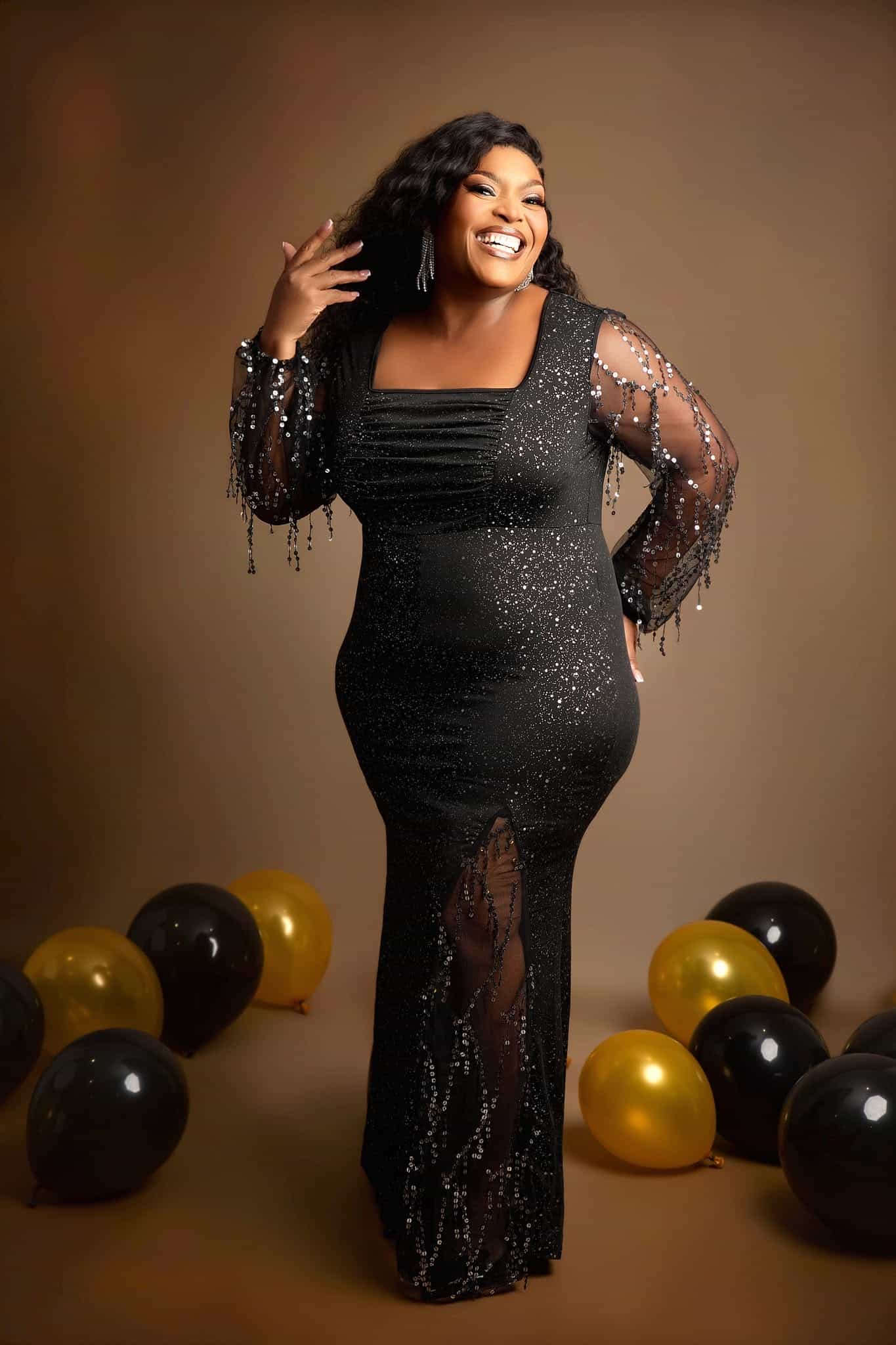 Woman in a black sequin dress with balloons on a brown background