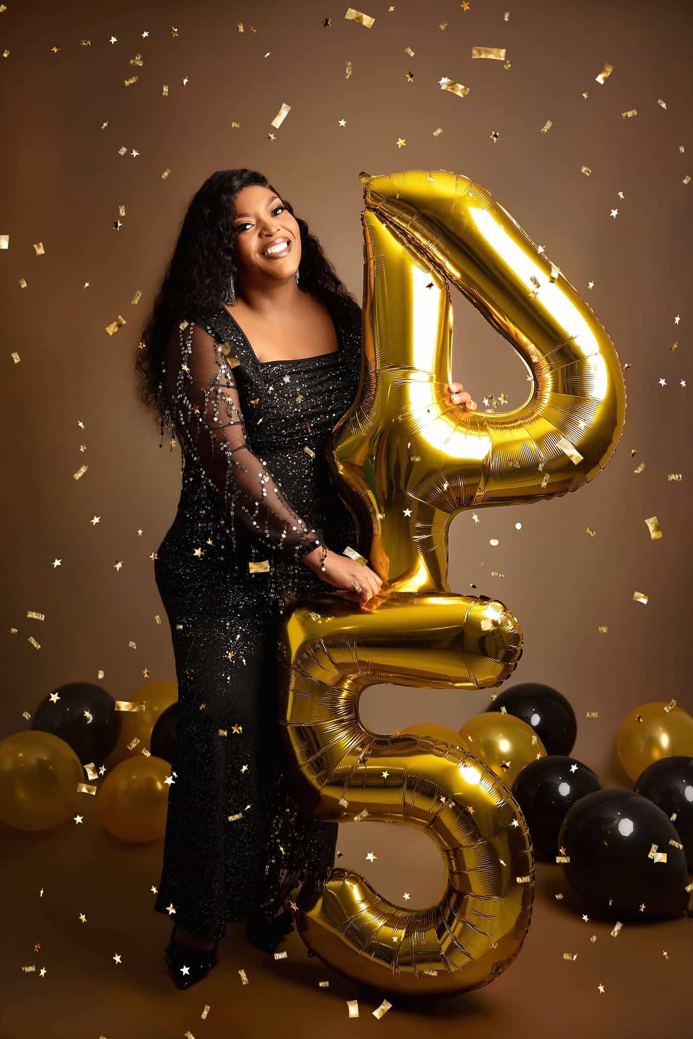 Woman holding a large gold number 45 balloon against a brown background with confetti.