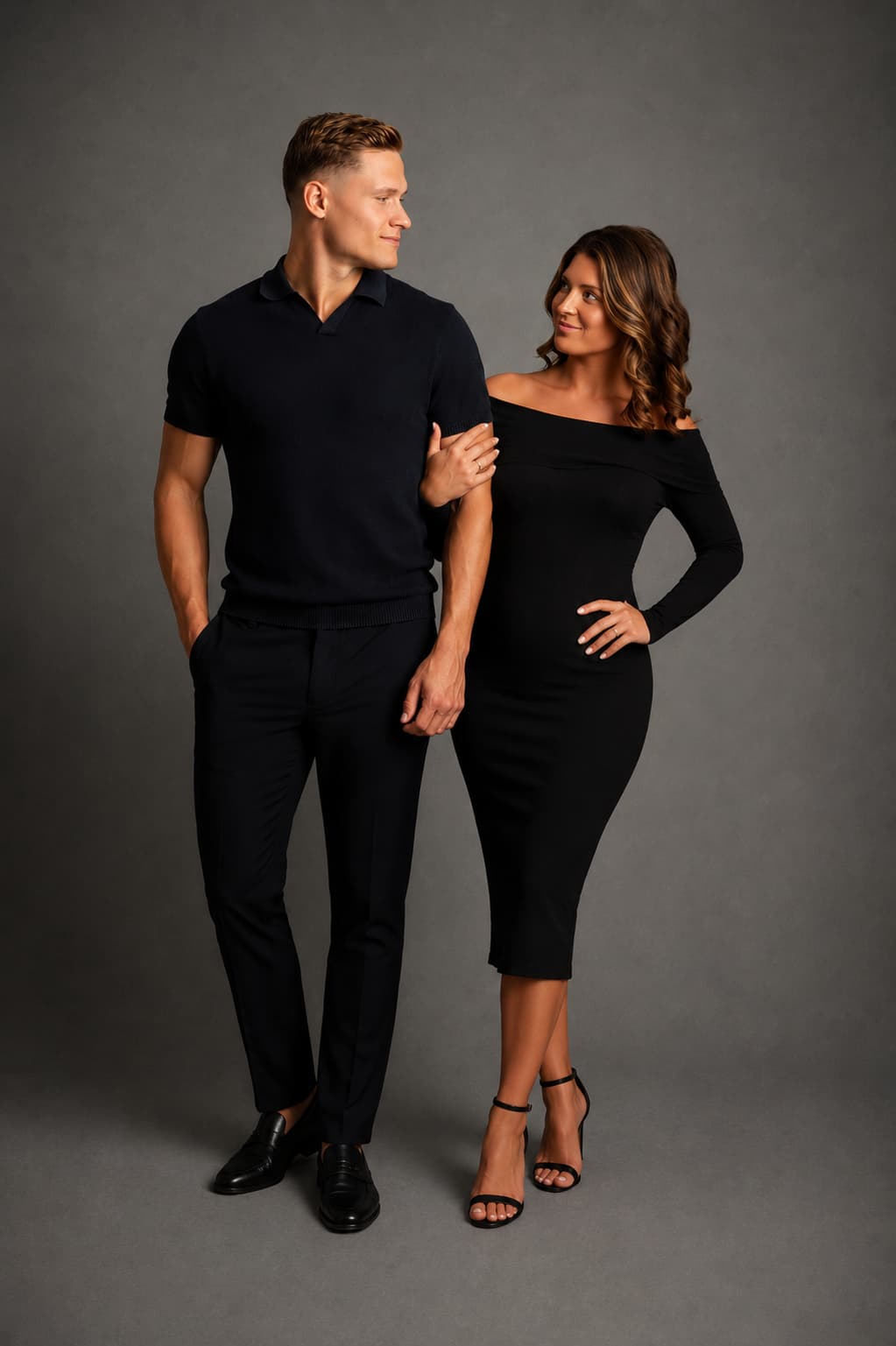 Man and woman in black outfits standing against a gray background