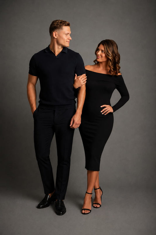 Man and woman in black outfits standing against a gray background