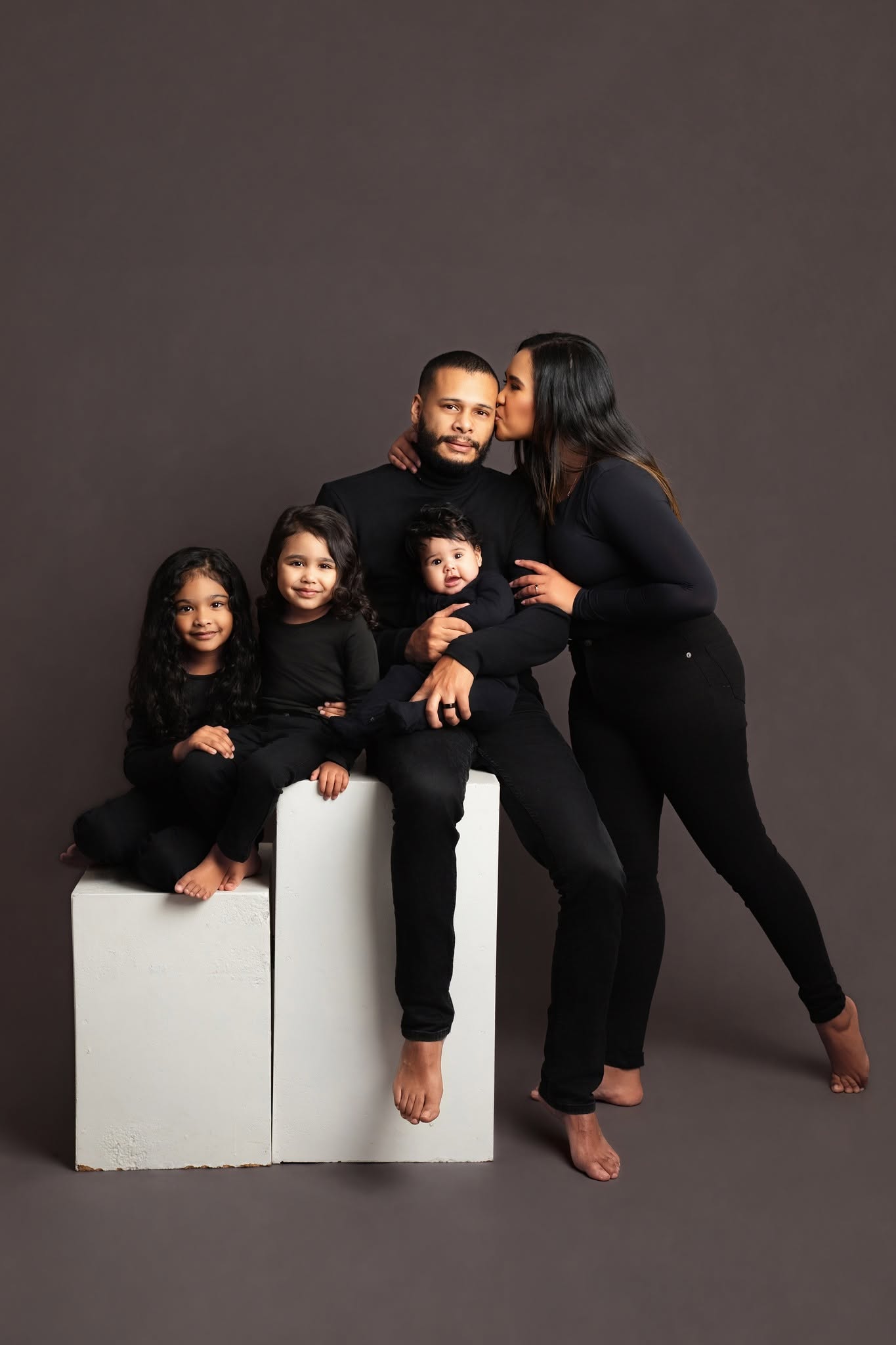 Family of five in black outfits posing on a gray background