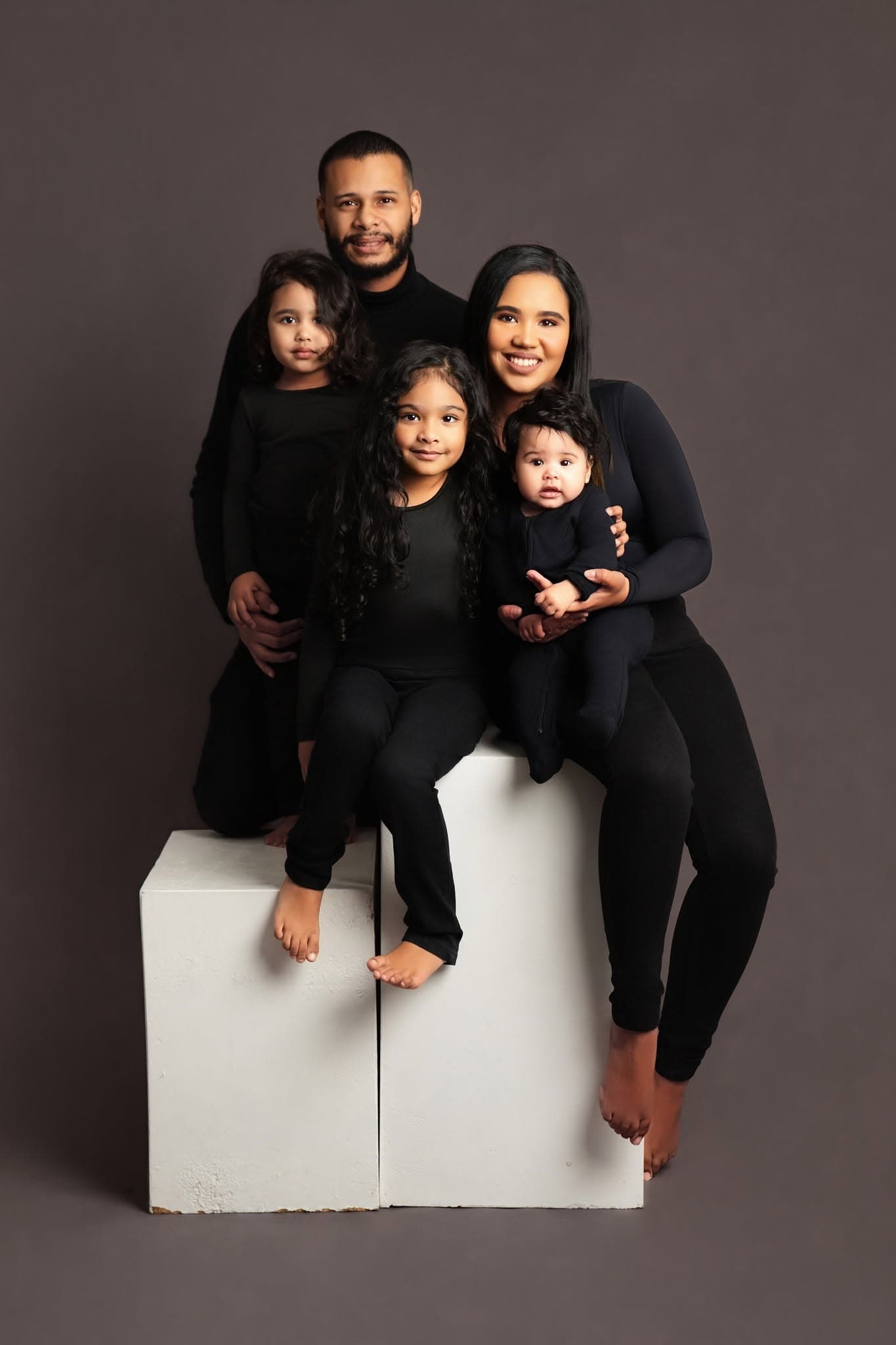 Family of five posing together on a white block against a dark background