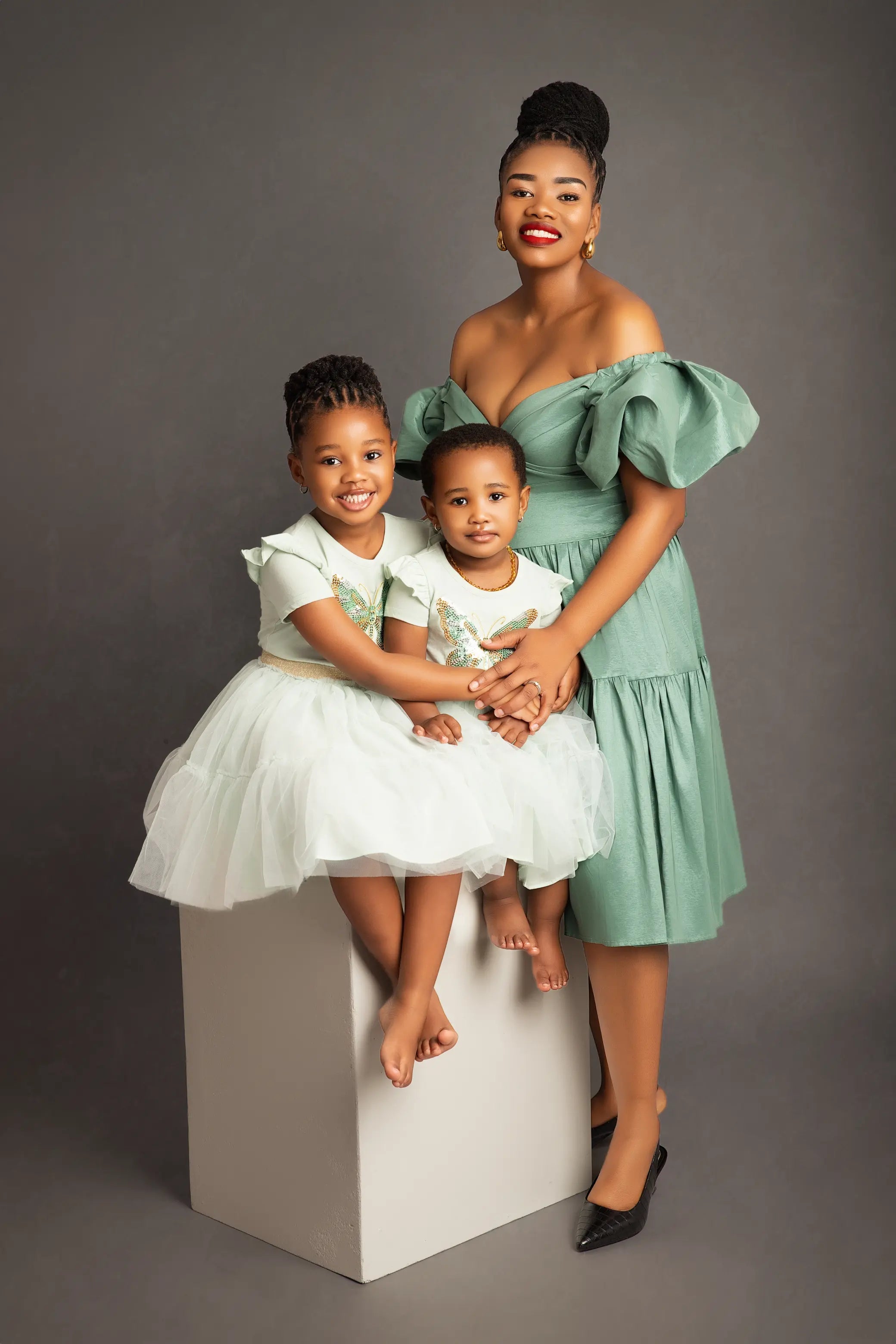 Woman in a green dress with two children in white dresses on a gray background