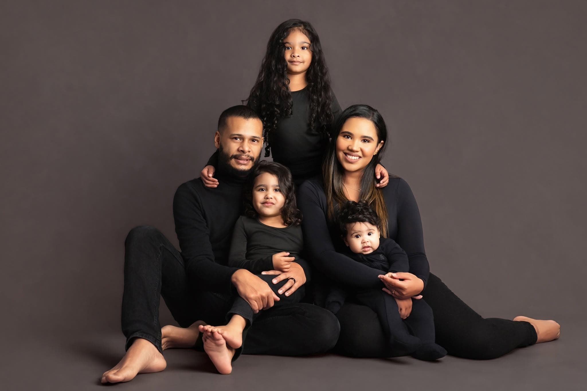 Family of 5 dressed in Black sitting on the floor posing for a family shoot
