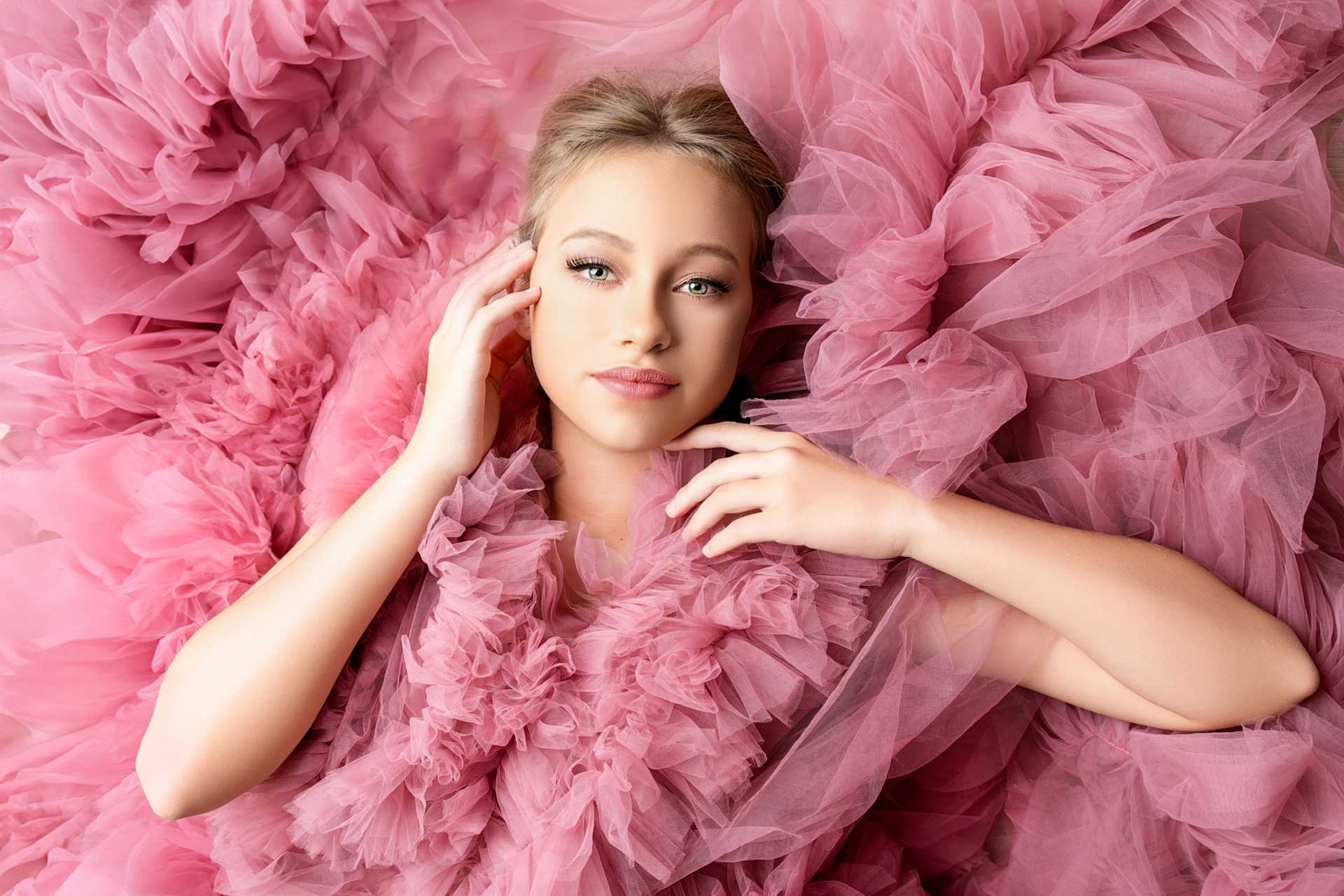 A stunning glamour beauty portrait of a model in a soft, fluffy pink dress, posing elegantly with a confident gaze at LiMia Photography studio in Brackenfell, Cape Town. The delicate fabric adds a dreamy, ethereal touch, enhancing the model's radiant beauty and showcasing timeless studio glamour photography.
