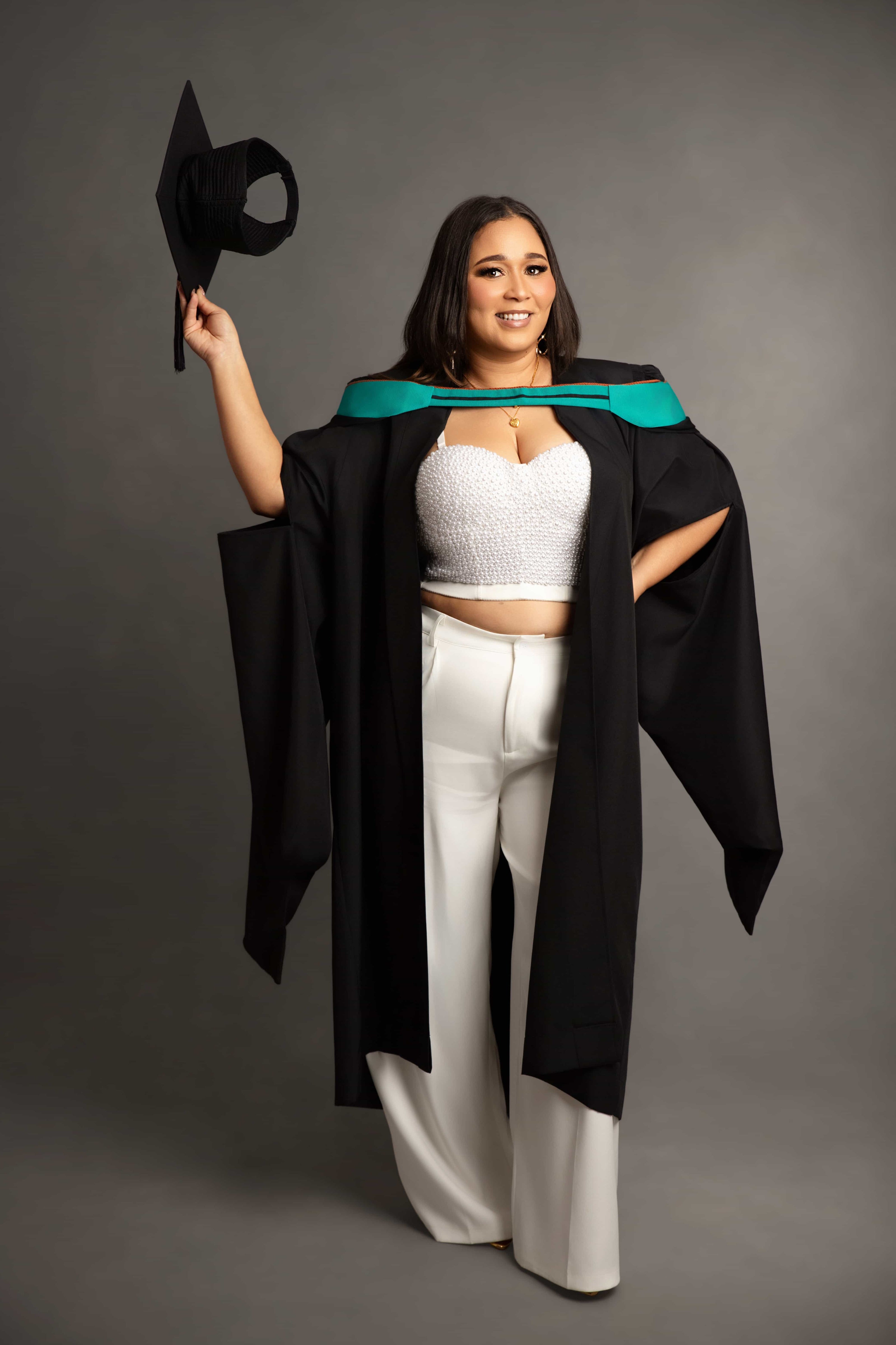 Woman in graduation gown holding a cap against a gray background