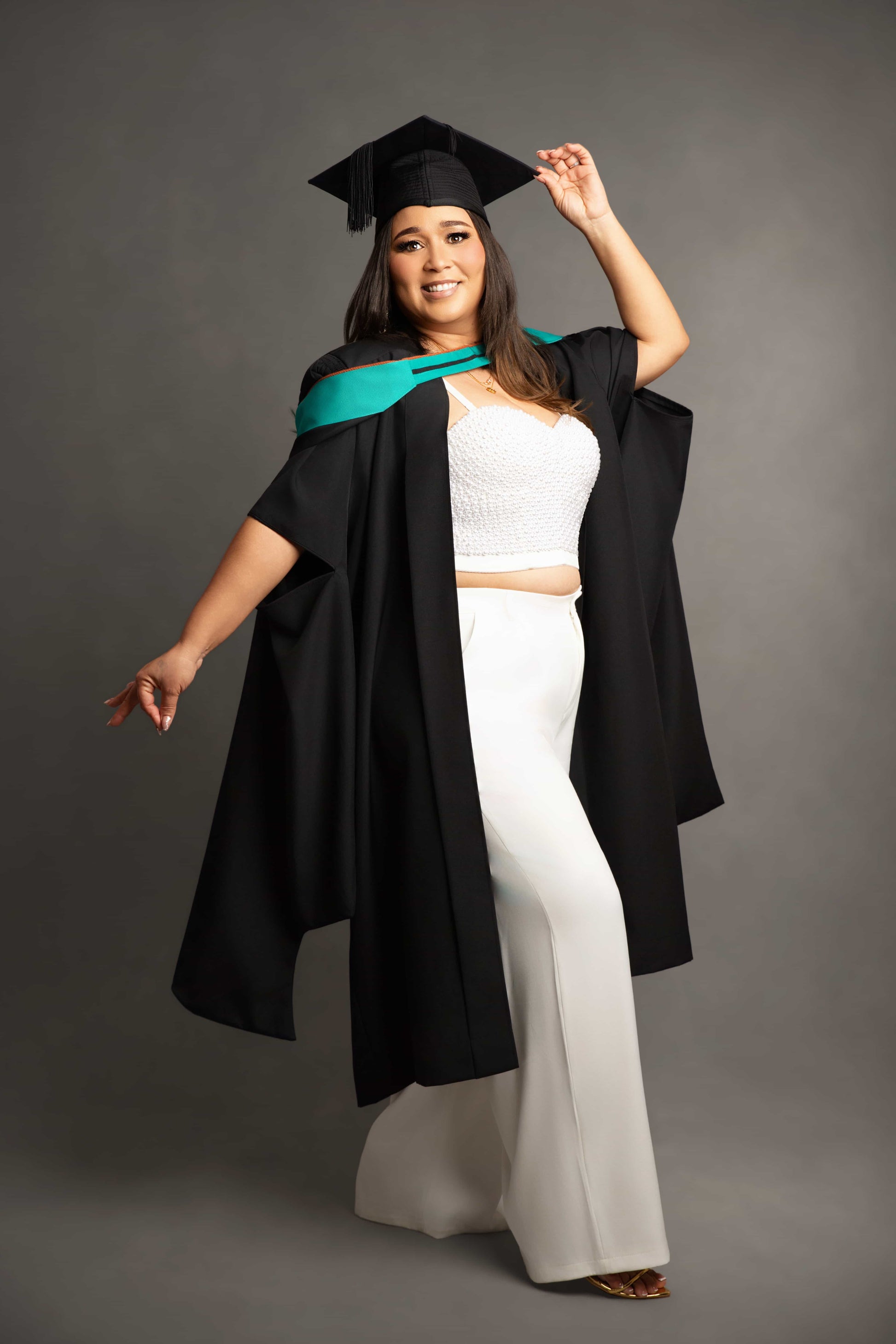 Person in graduation gown and cap with a teal stole on a gray background