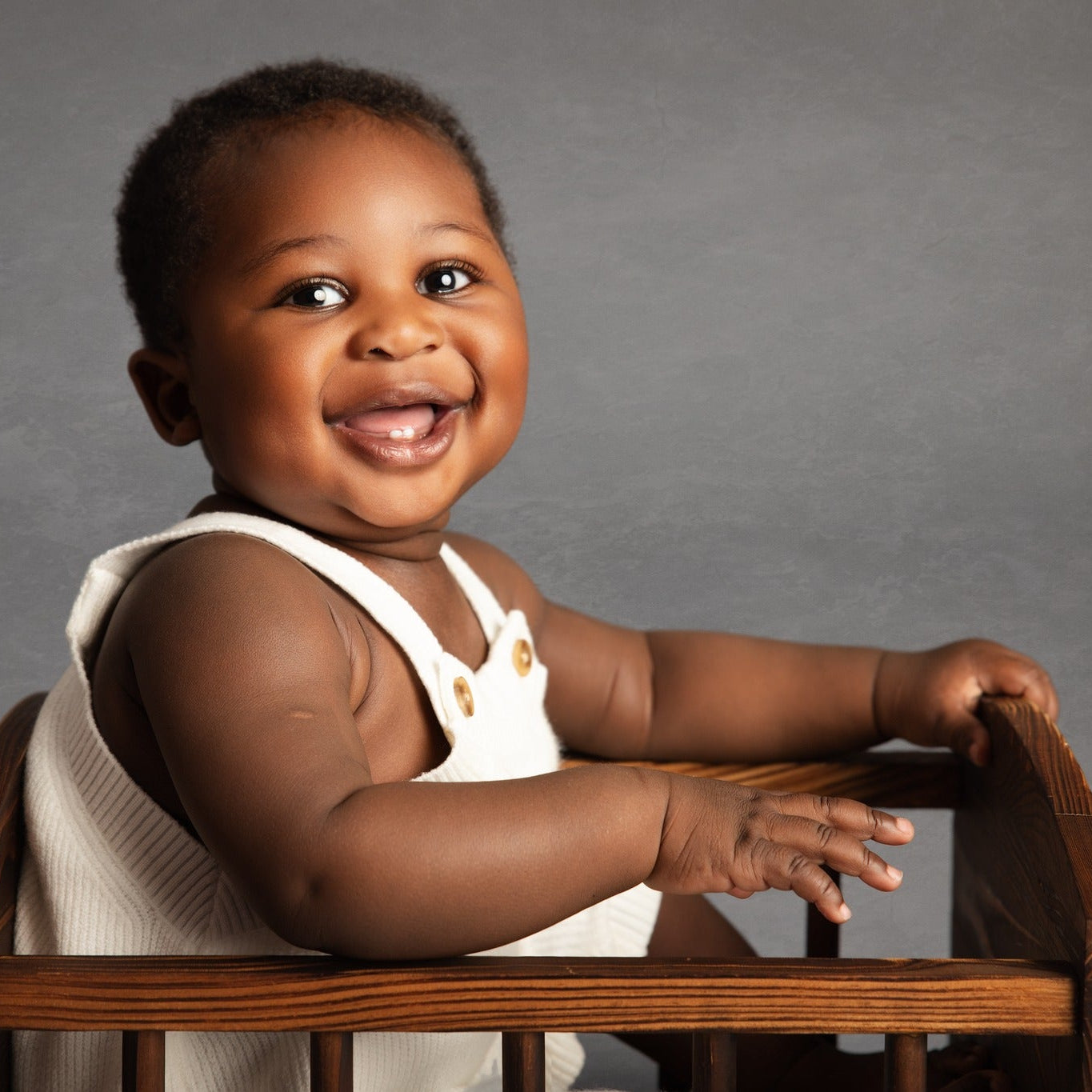 Child sitting in a wooden high chair against a gray background