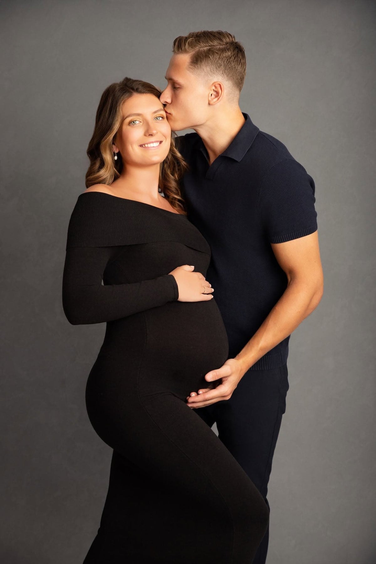Pregnant woman in a black dress with a man on a gray background