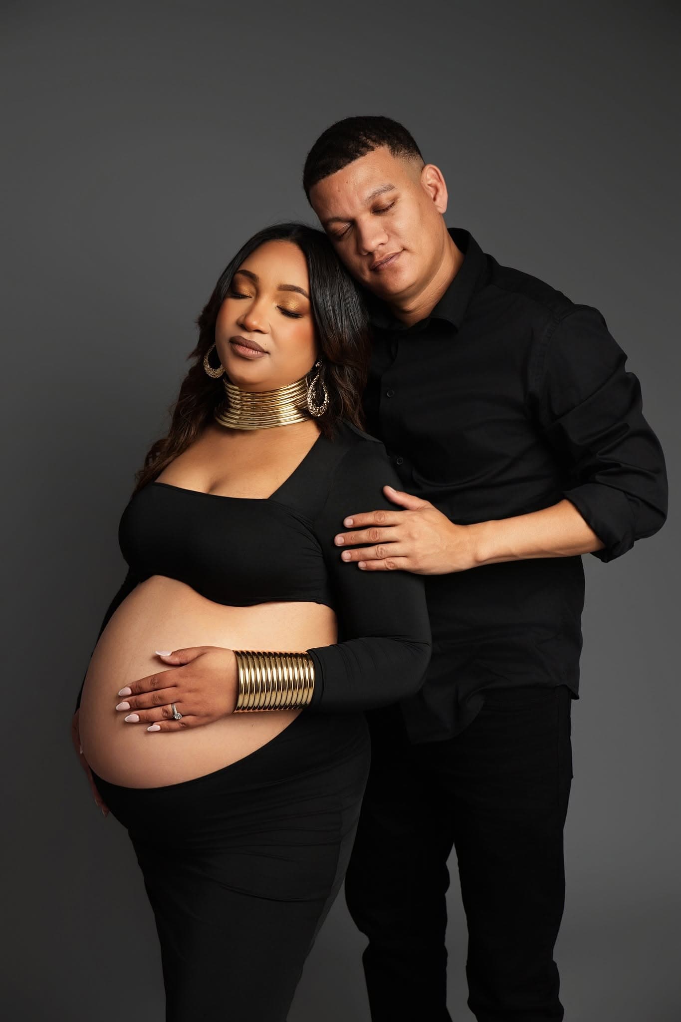 Pregnant woman and a man embracing against a dark background