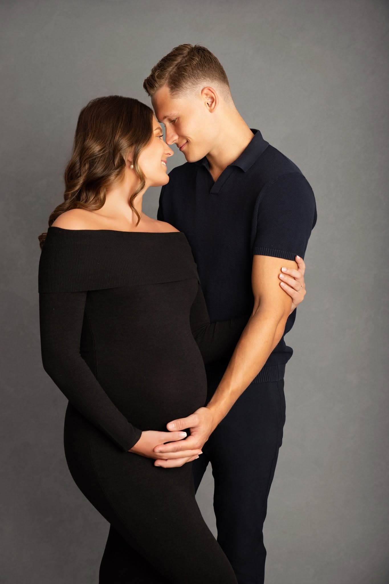 Pregnant woman and man embracing against a gray background