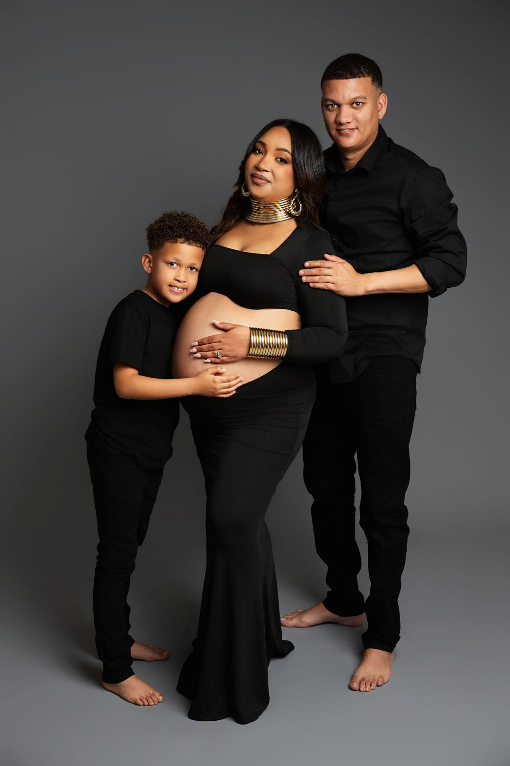 Family of four in black outfits against a gray background during a maternity photo shoot
