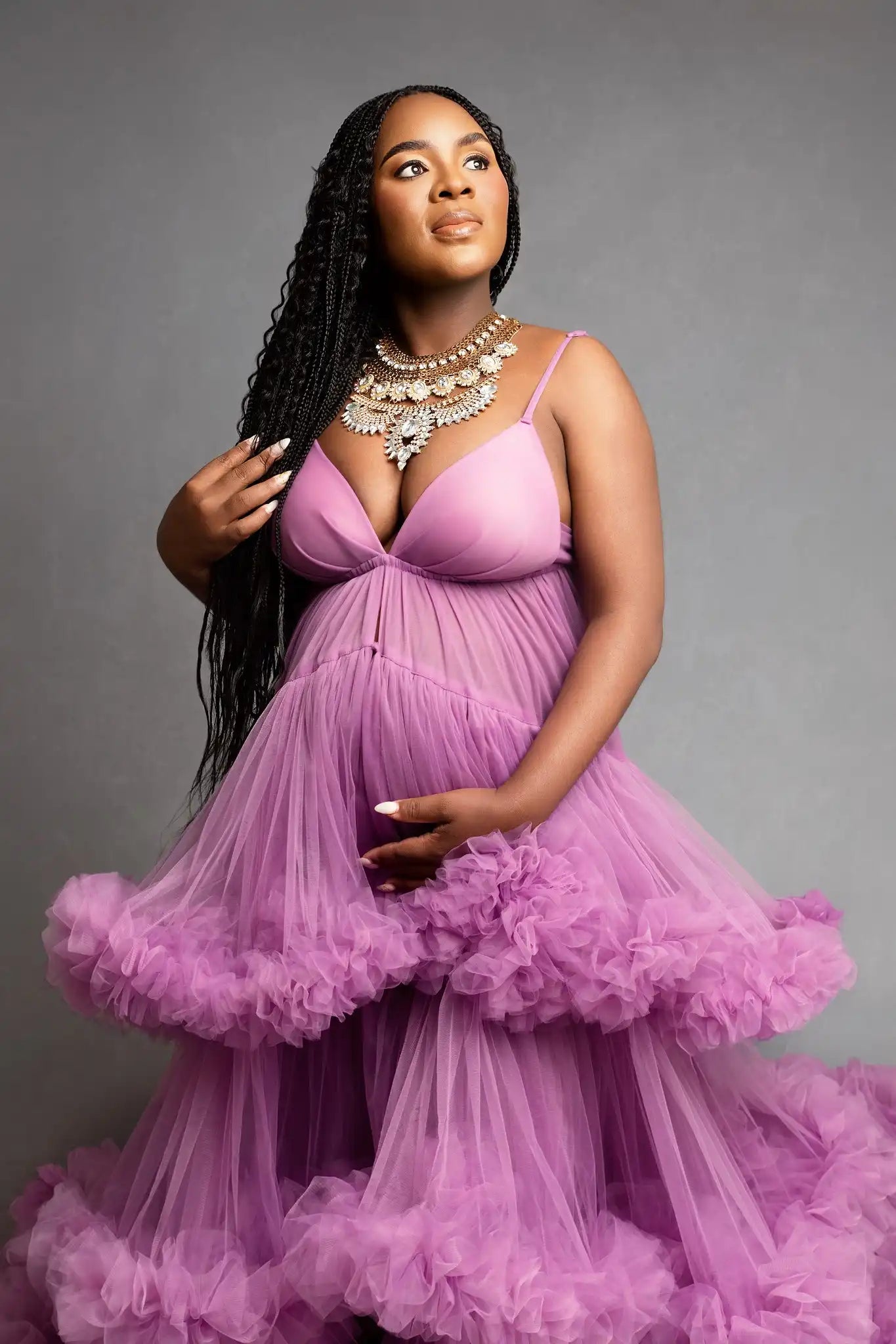Woman wearing a purple dress with ruffled layers against a gray background during her maternity photo shoot