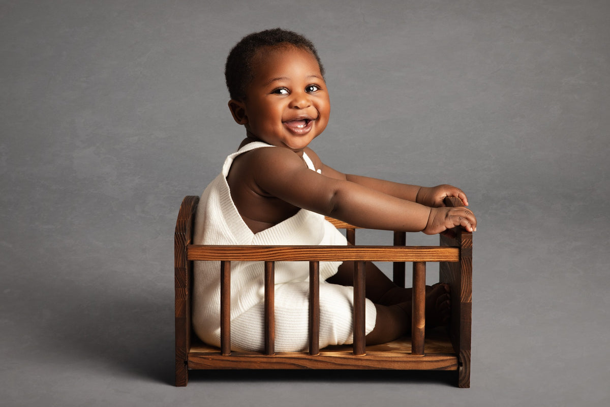 Child sitting on a small wooden bed against a gray background