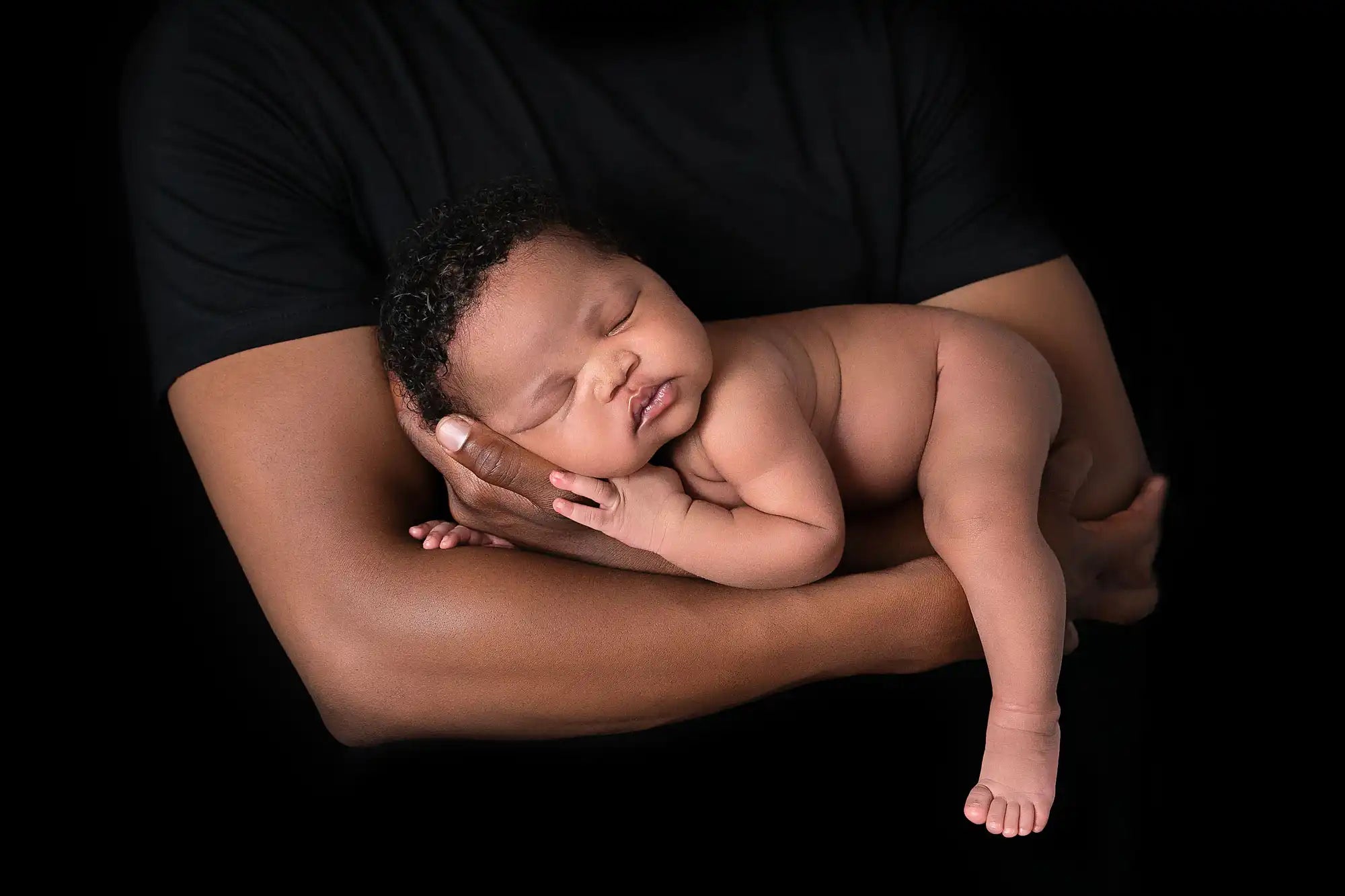 Newborn baby being held by an adult against a black background