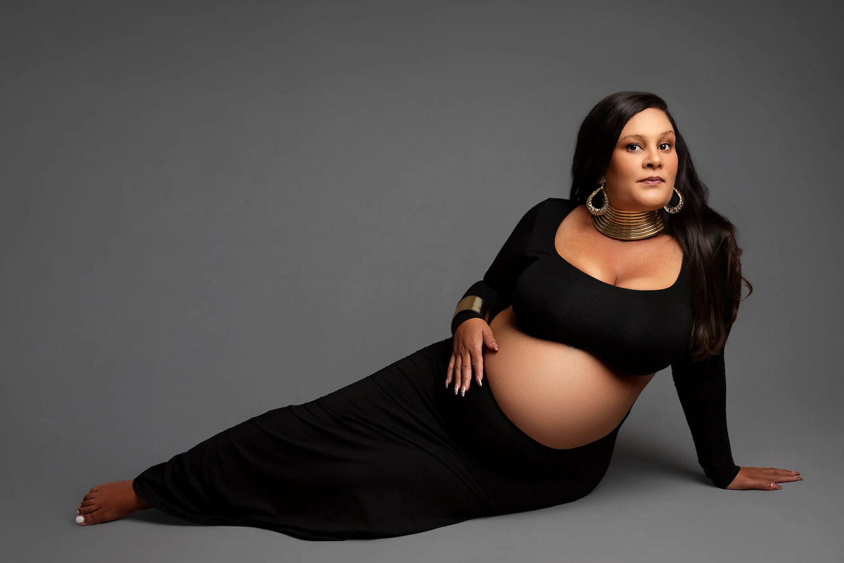 Pregnant woman in a black dress posing on a gray background