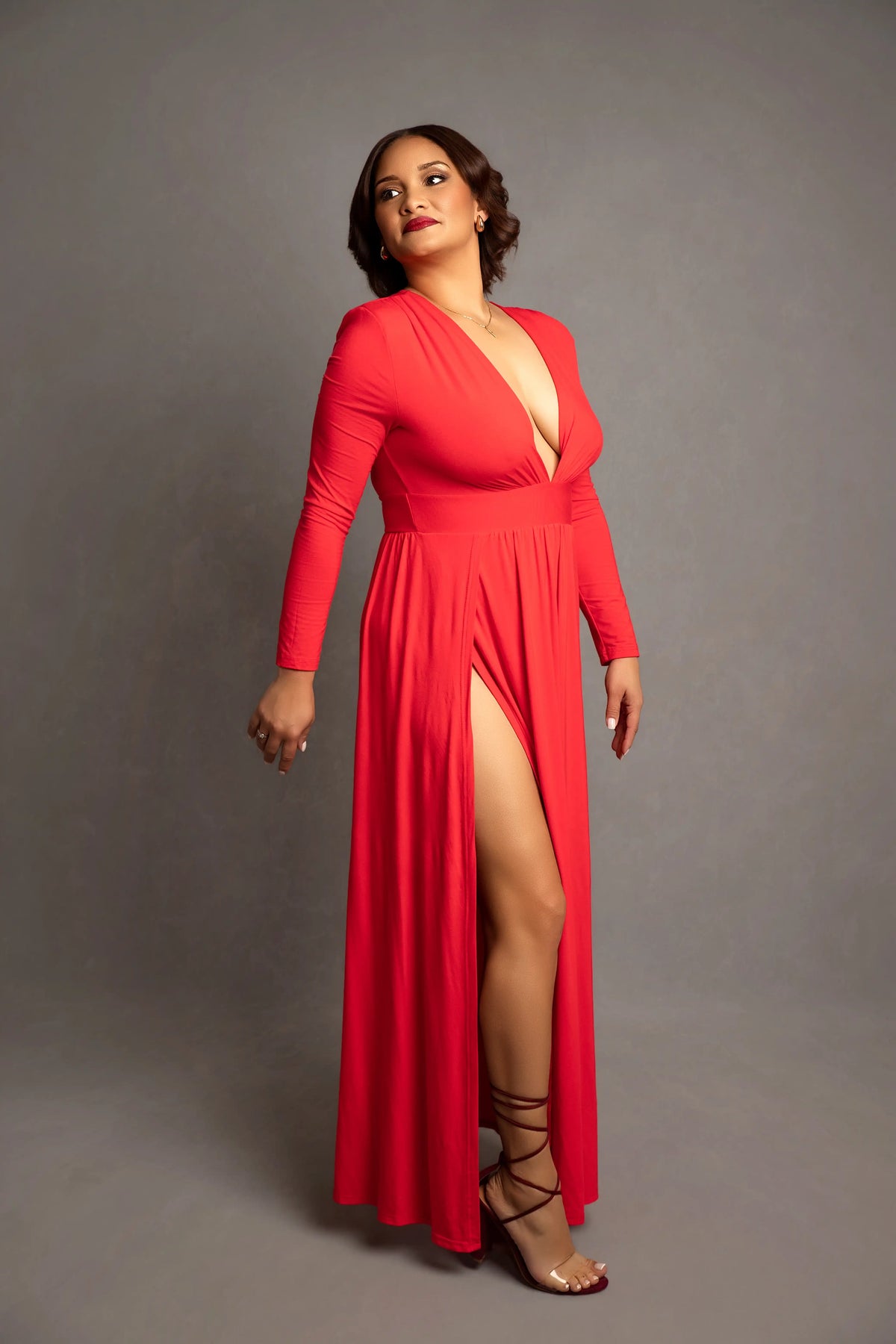 Woman wearing a red dress with a slit on a gray background
