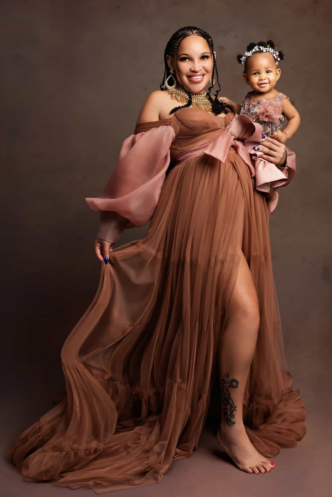 Woman in a long, flowing dress holding a child against a brown background